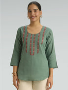 Woman wearing a green embroidered top against a plain background