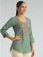 Woman wearing a green top with red embroidery on a light gray background