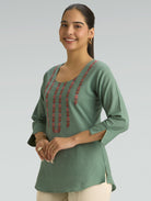 Woman wearing a green top with red embroidery on a gray background
