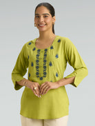 Woman wearing a green embroidered top against a gray background