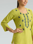 Woman wearing a green embroidered top against a gray background