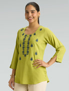 Woman wearing a green embroidered top on a gray background