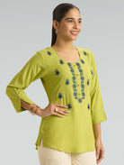 Woman wearing a green embroidered top against a gray background