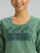 Green embroidered top worn by a person on a gray background