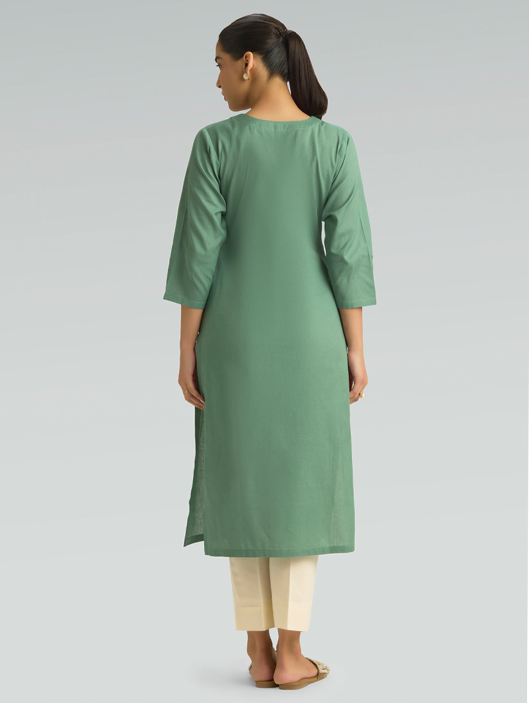 Woman wearing a green kurta with beige pants on a light gray background