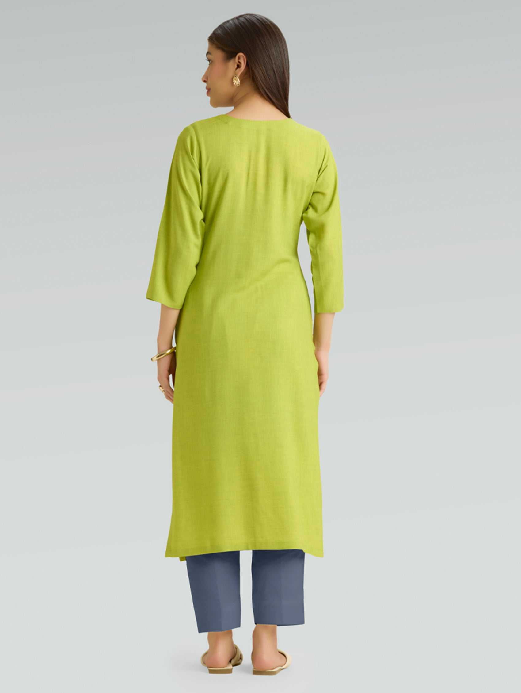 Woman wearing a green kurta with blue pants on a light gray background