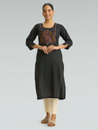 Woman wearing a black kurta with intricate embroidery on a gray background