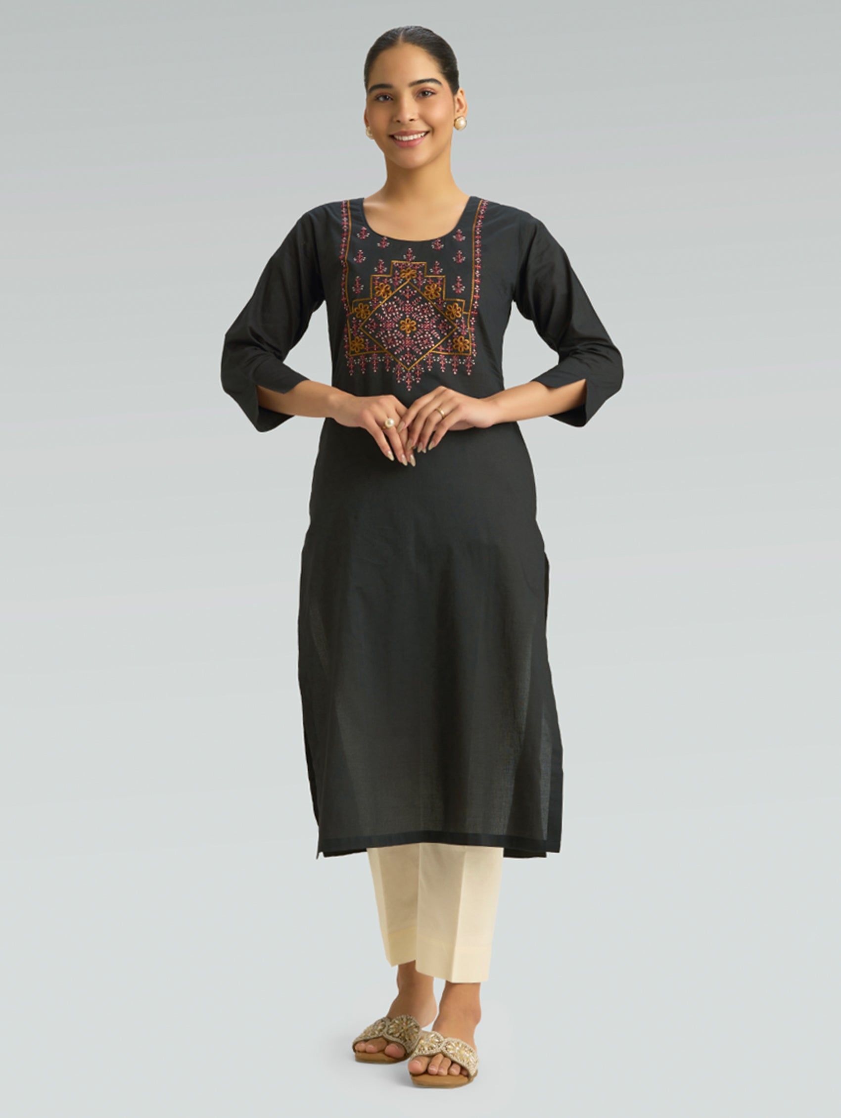 Woman wearing a black kurta with intricate embroidery on a gray background