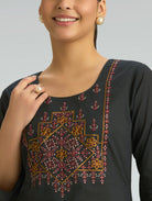 Woman wearing a black top with intricate floral embroidery on a plain background