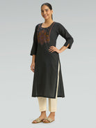Woman wearing a black kurta with embroidery on a gray background