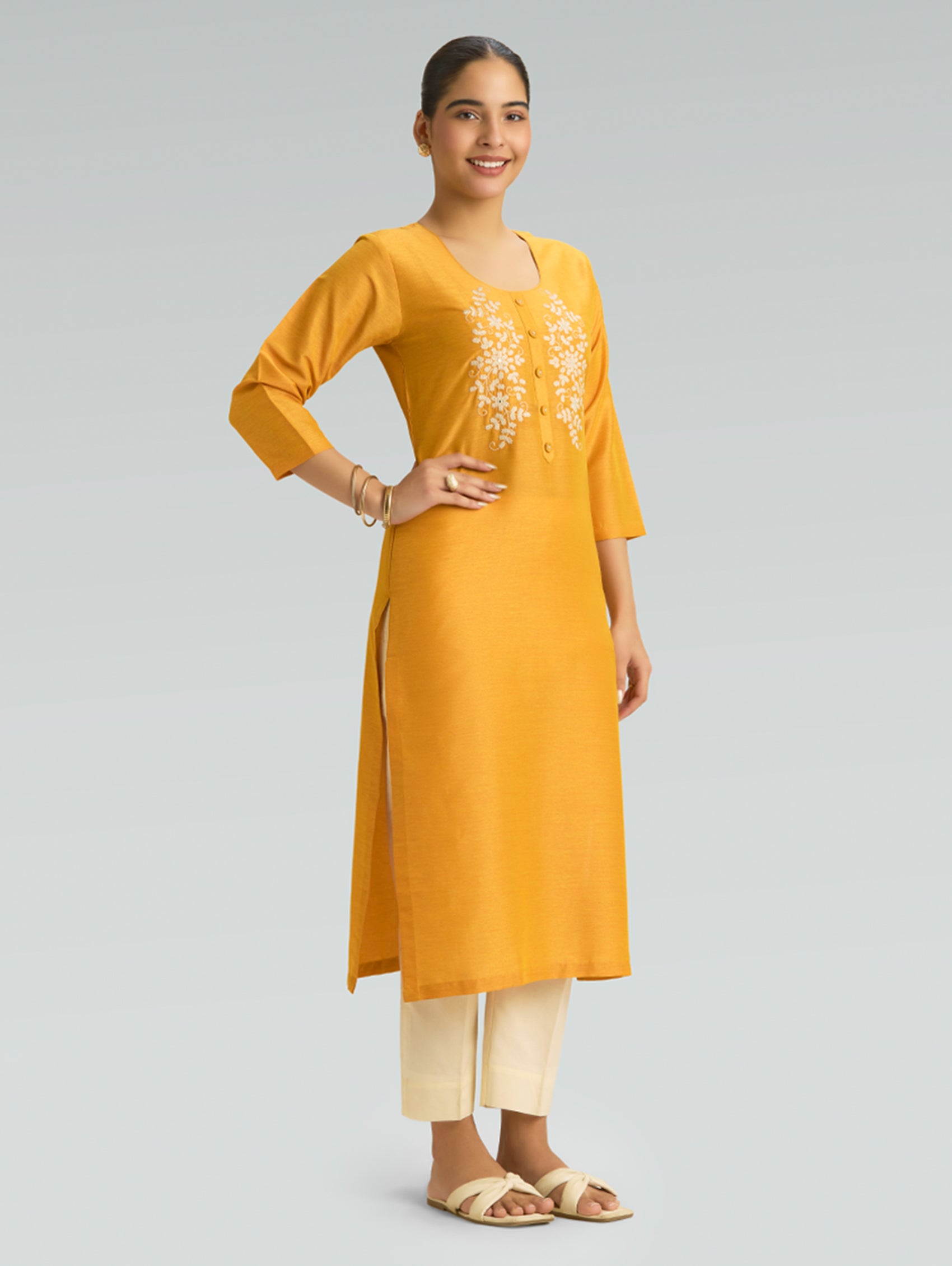 A woman wearing a Moon yellow kurta with side slit and white pants on a gray background