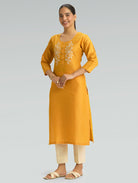 Woman wearing a moon yellow kurta with white embroidery on a gray background