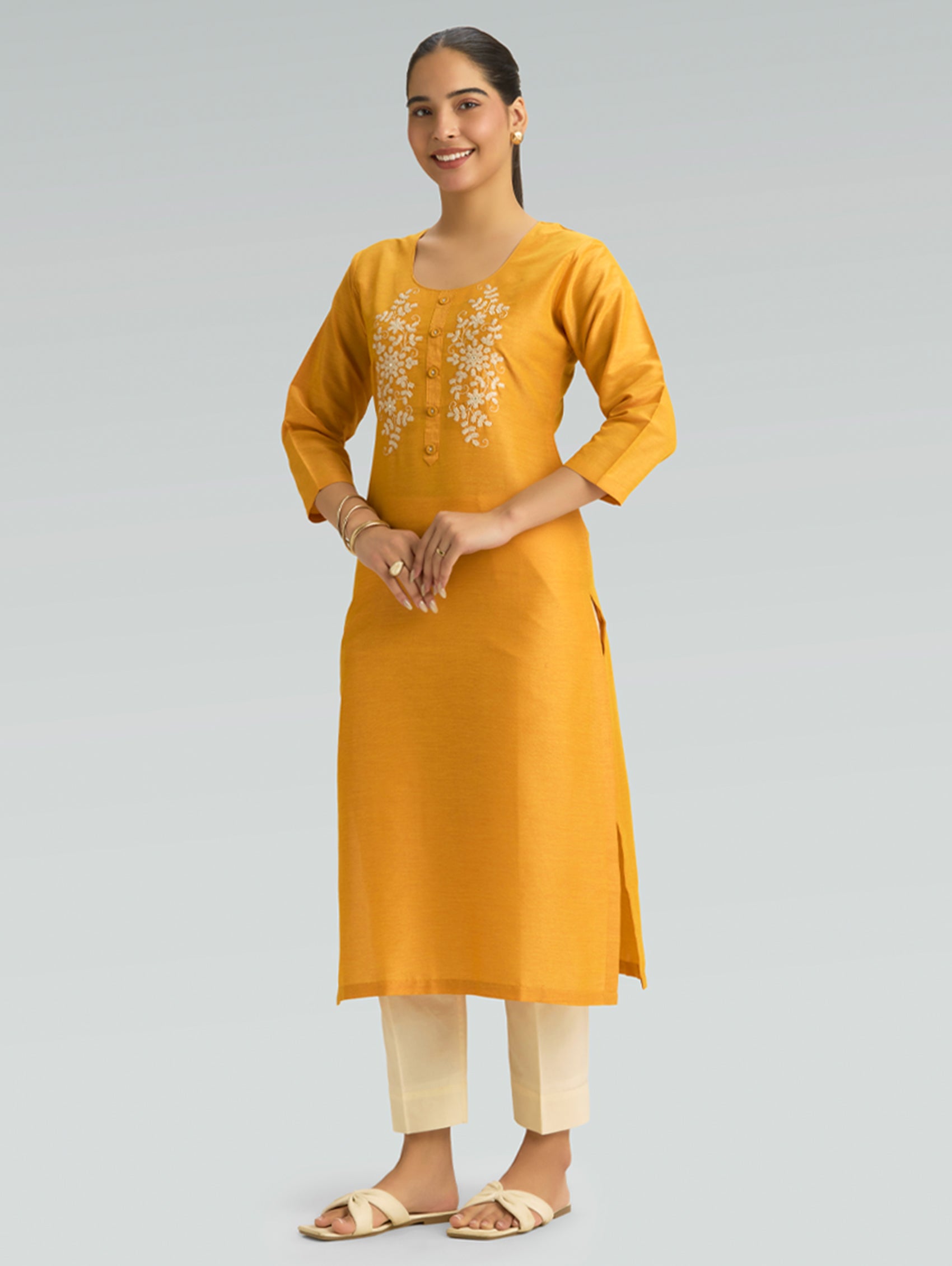 Woman wearing a moon yellow kurta with white embroidery on a gray background