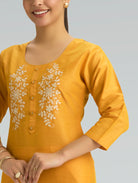 Woman wearing a yellow kurta with floral embroidery and 3/4 sleeves on a grey background