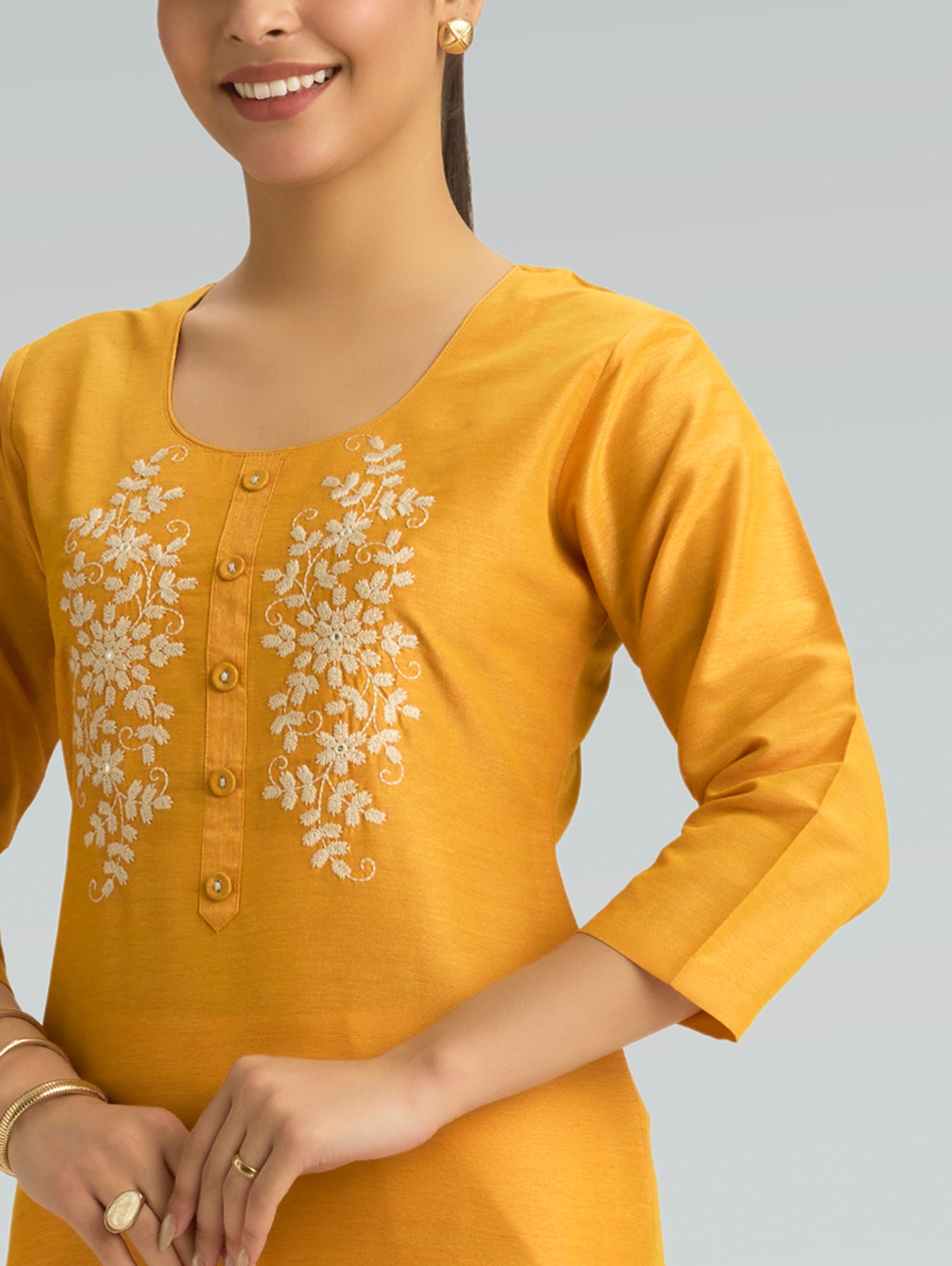 Woman wearing a yellow kurta with floral embroidery and 3/4 sleeves on a grey background