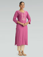 A woman is wearing a pink kurta with white embroidery and a side slit, along with 3/4 sleeves, against a grey background.