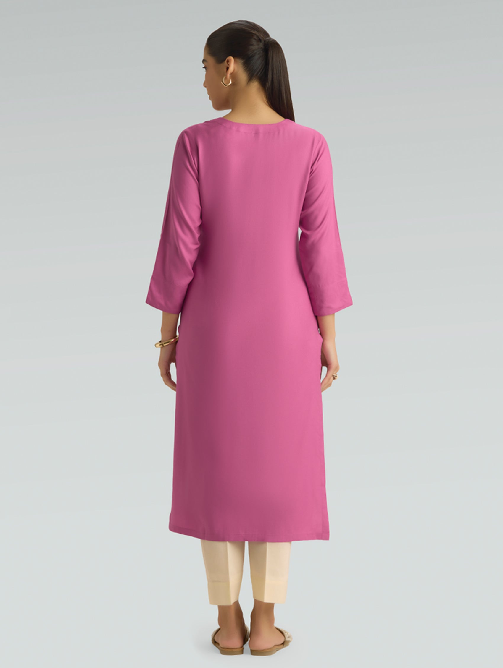A woman is wearing a pink kurta for women, featuring a plain back design and a comfortable straight-fit silhouette.