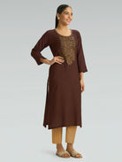 Woman wearing a brown kurta with intricate embroidery on a light gray background