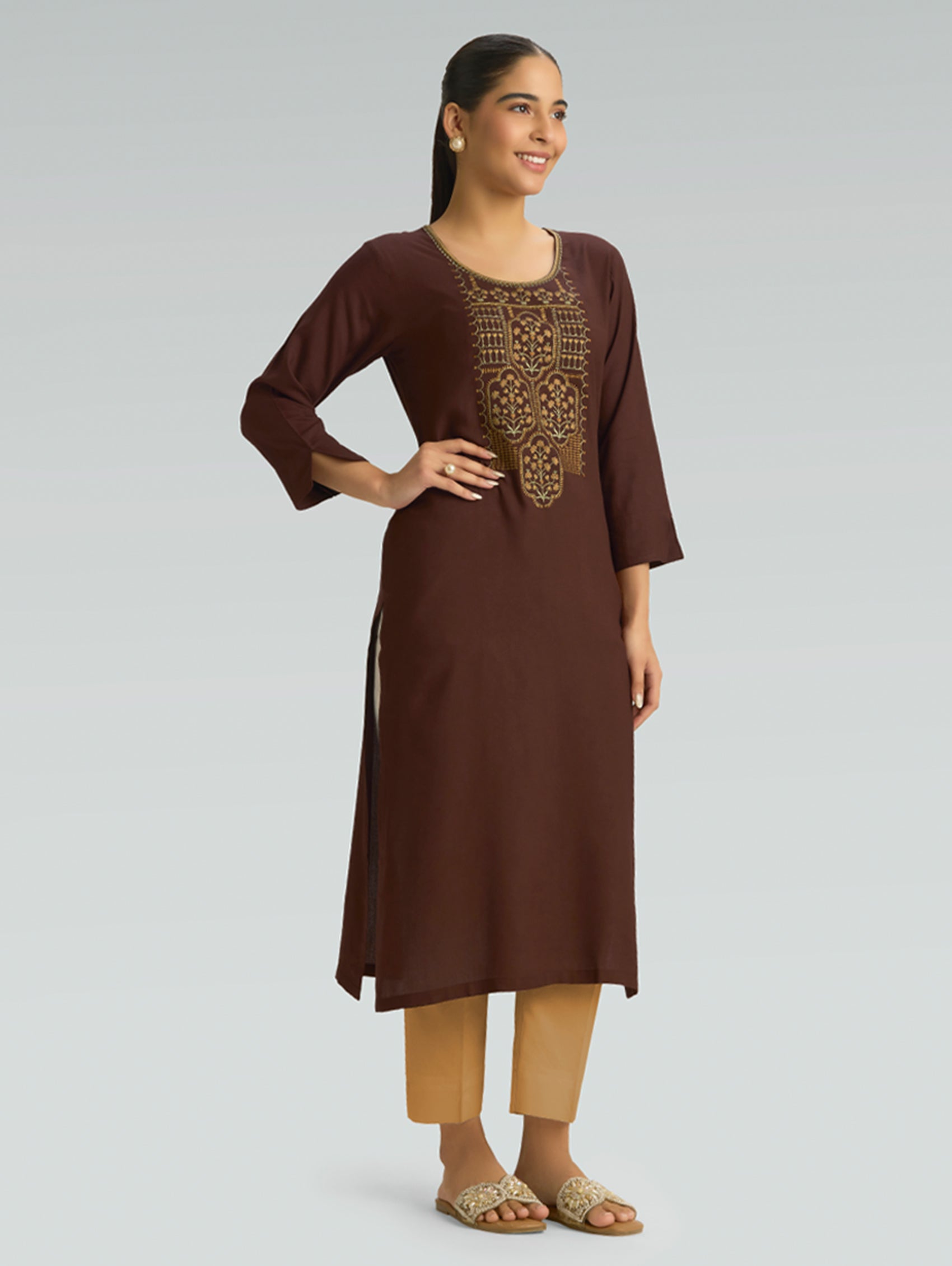 Woman wearing a brown kurta with intricate embroidery on a light gray background