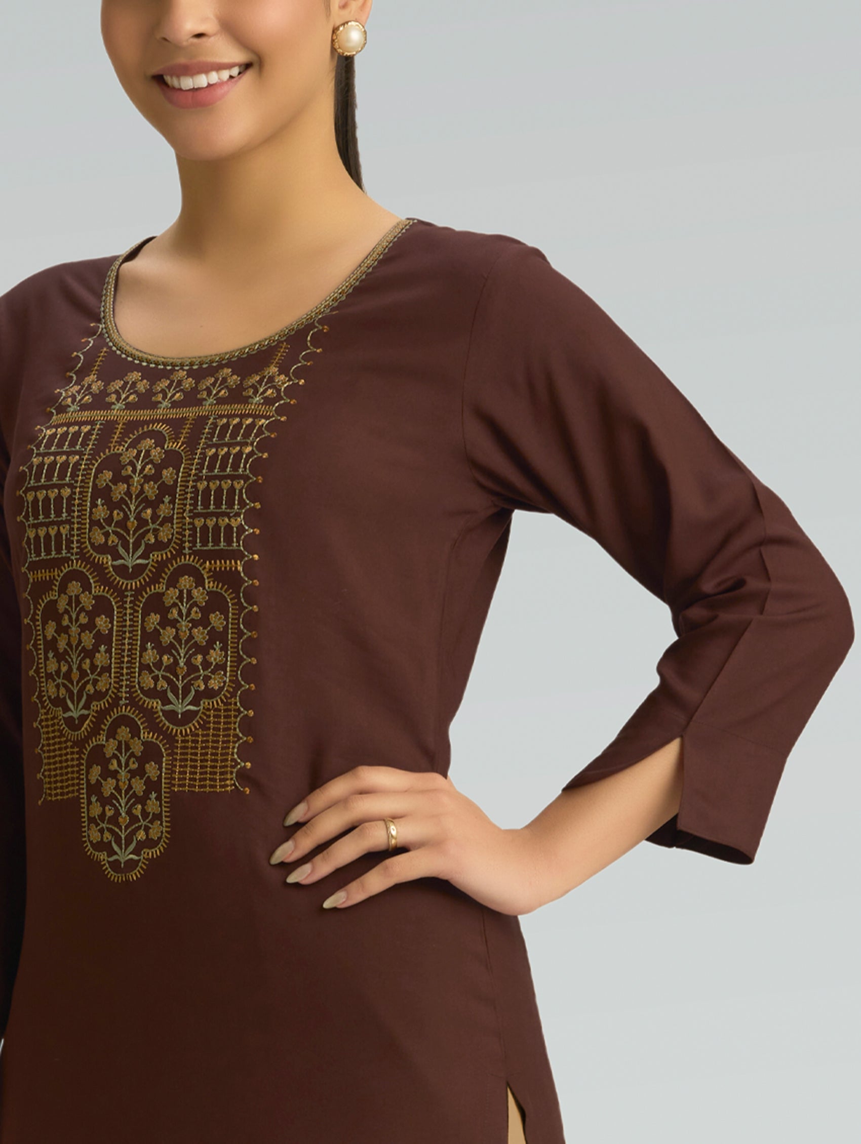 Woman wearing a brown dress with intricate gold embroidery with 3/4 sleeves on a plain background