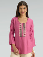 Woman wearing a pink embroidered top on a gray background