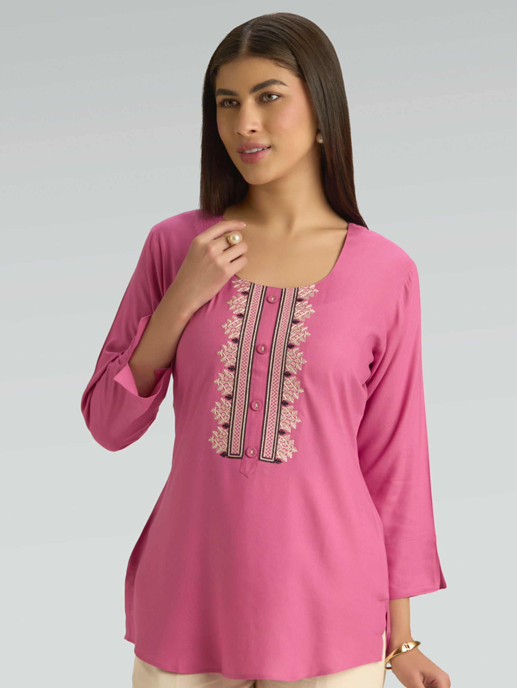 Woman wearing a pink embroidered kurti against a gray background