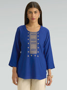 Woman wearing a blue embroidered top on a gray background
