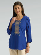 Woman wearing a blue embroidered top on a gray background