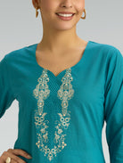 Teal top with intricate white embroidery on a plain background