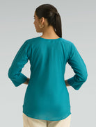 Woman wearing a teal long-sleeve top on a gray background