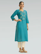 Woman wearing an Iris Blue embroidered kurta with white pants on a light gray background