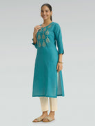 Woman wearing an Iris Blue embroidered kurta with beige pants on a light grey background