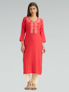 Woman wearing a red kurta with white embroidery on a gray background
