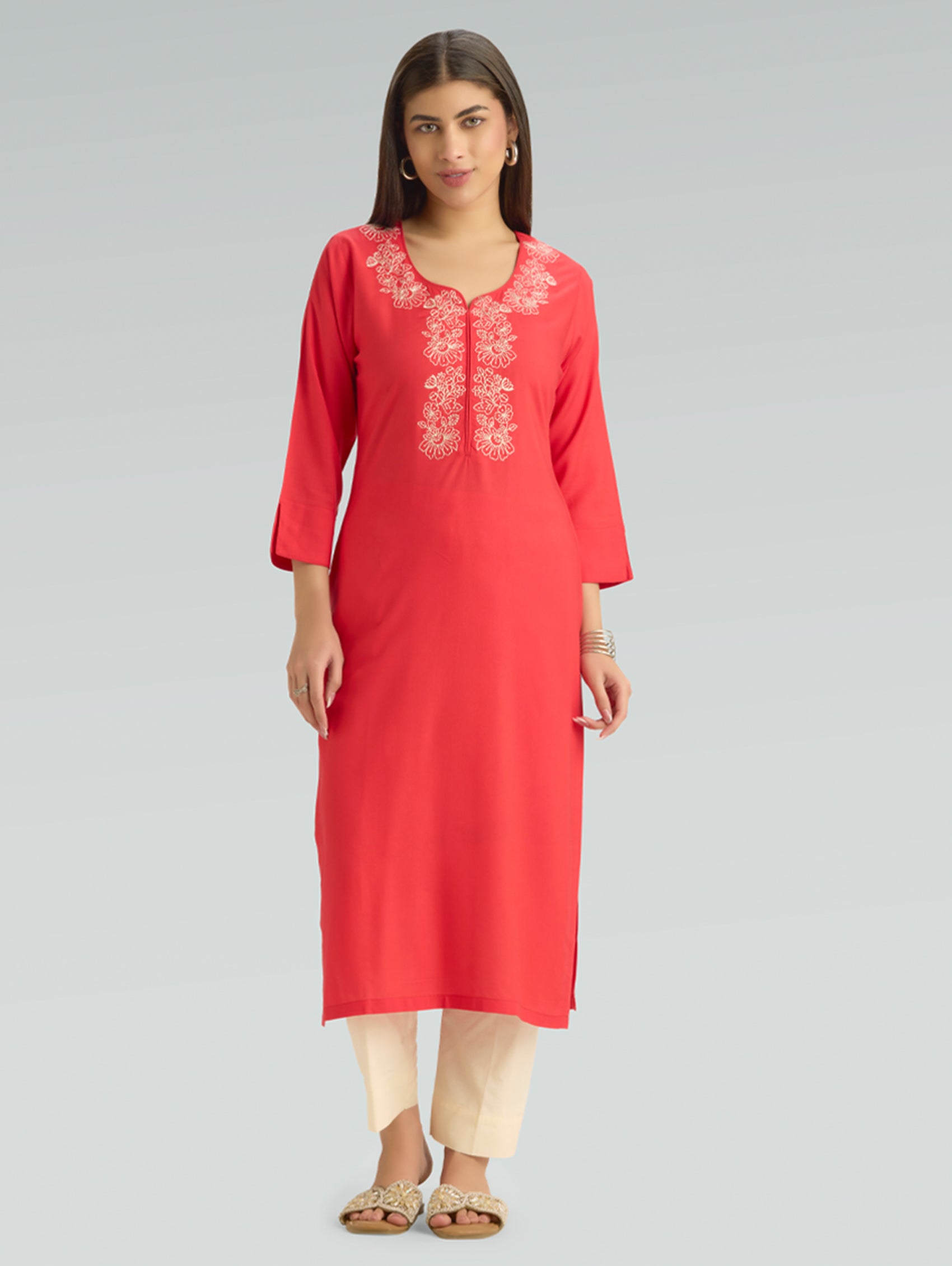 Woman wearing a red kurta with white embroidery on a gray background