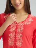 Red top with white floral embroidery worn by a model against a neutral background