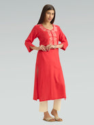 Woman wearing a red kurta with white embroidery on a gray background