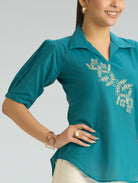Woman wearing a teal polo shirt with floral embroidery on a plain background