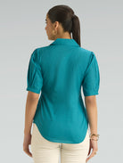 Woman wearing a teal shirt and beige pants on a gray background