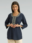 Woman wearing a navy blue embroidered top on a gray background