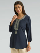 Woman wearing a navy blue embroidered top on a gray background