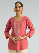 Woman wearing a pink embroidered top on a gray background