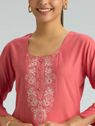 Woman wearing a pink top with white embroidery on a gray background