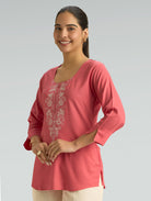 Woman wearing a pink embroidered top against a gray background