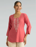 Woman wearing a pink embroidered top against a gray background
