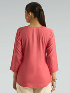 Person wearing a pink top with three-quarter sleeves on a gray background