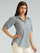 Woman wearing a patterned shirt and white pants on a gray background