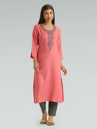 Woman wearing a flamingo pink kurta with a round neckline and intricate computer embroidery with side slit on a grey background