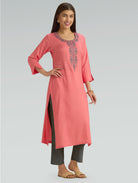 Woman wearing a flamingo pink kurta with a round neckline and intricate computer embroidery with side slit on a grey background