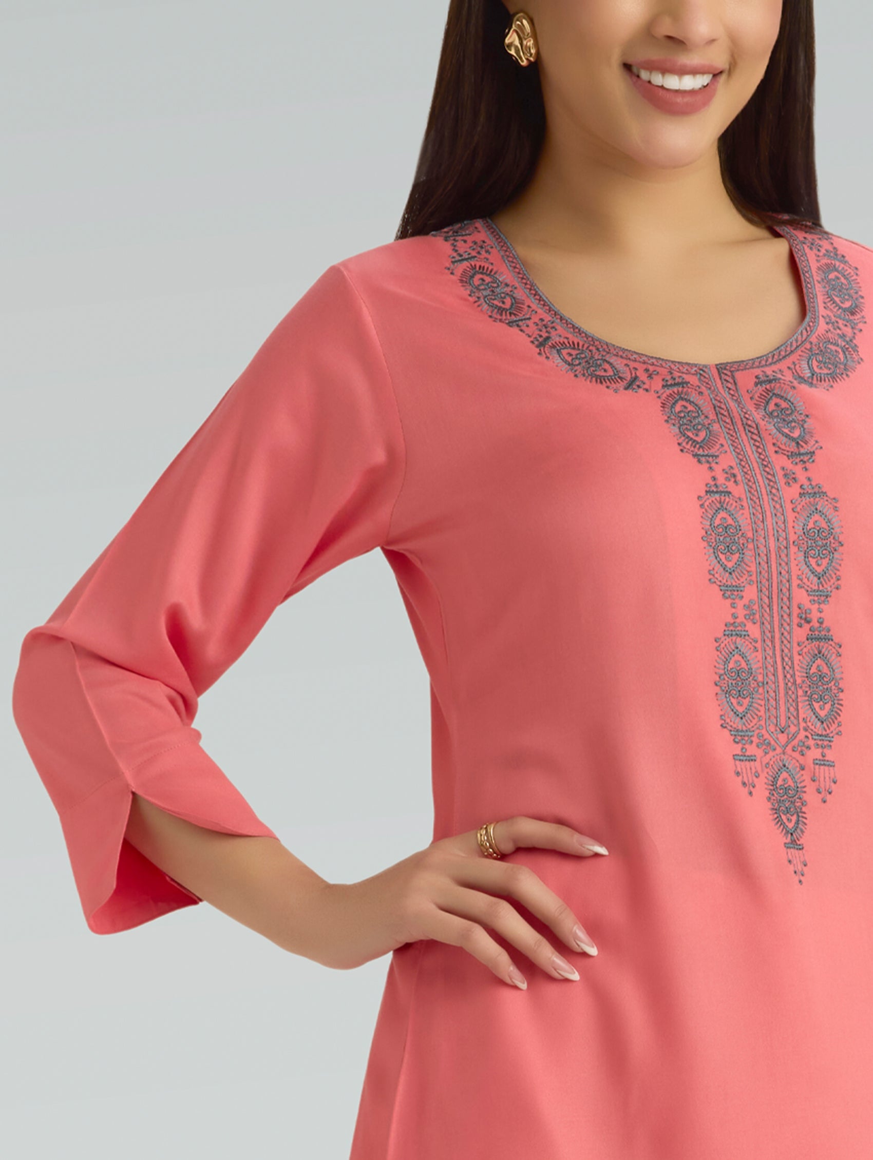 Woman wearing a flamingo pink dress with intricate embroidery on a plain background