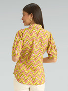 Woman wearing a yellow and pink zigzag patterned blouse against a gray background